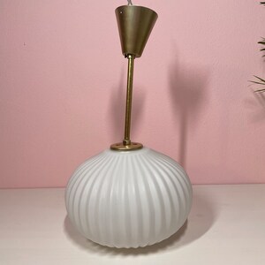 May include: A white ribbed glass pendant light with a brass ceiling mount and a brass rod.