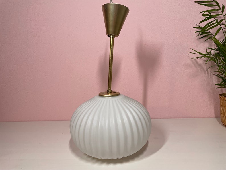 May include: A white ribbed glass pendant light with a brass ceiling mount and a brass rod.