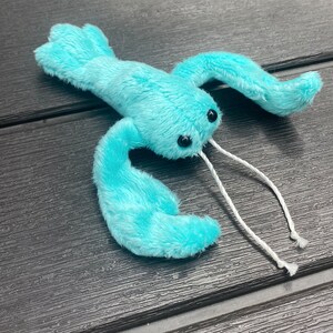 May include: A turquoise blue plush lobster toy with white string antennae. The lobster has black eyes and is made of soft, fuzzy fabric.
