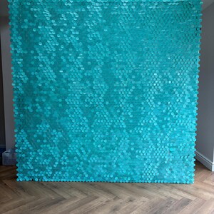May include: A large turquoise wall decoration made up of many hexagonal shapes. The wall art is a vibrant teal colour and stands upright. The background features a wooden floor.