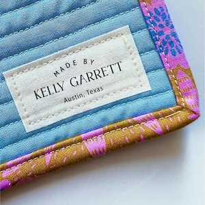 Puede incluir: Primer plano de una tela azul y rosa con una etiqueta blanca que dice "MADE BY KELLY GARRETT Austin, Texas".