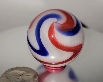 May include: A white glass marble with red and blue swirls. The marble is about the size of a US quarter.