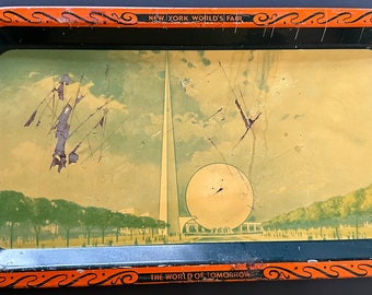 May include: A vintage metal tray with an orange border and black interior. The tray features a faded image of the 1939 New York World's Fair, including the Trylon and Perisphere, with the text "NEW YORK, WORLD'S FAIR" and "THE WORLD OF TOMORROW".