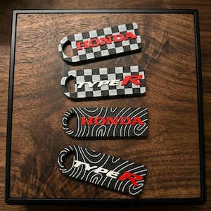 May include: Four keychains with the Honda and Type R logos. Two keychains have a black and white checkered pattern, and two have a black and white topographic pattern. The logos are in red.