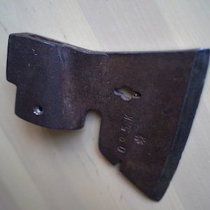 Peut inclure: Une tête de hache en métal rouillée avec un petit trou dans la lame et le texte "08 51 K" estampillé sur le côté.