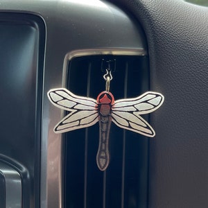 May include: A white and red dragonfly car air freshener hanging from a car's air vent.