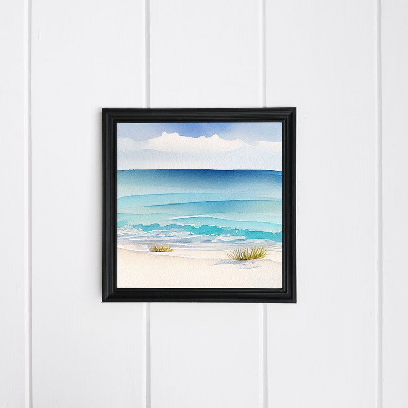Puede incluir: Una pintura de acuarela enmarcada de una escena de playa. La obra de arte representa un oc&eacute;ano sereno con tonos de azul y turquesa, una playa arenosa y un cielo nublado. La pintura est&aacute; encerrada en un marco negro y montada en una pared blanca.