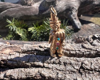 May include: A gold-colored charm of a jester with a red, green, and blue gemstone design.