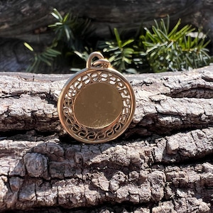 May include: A gold-colored pendant with a circular design. The pendant has a smooth, flat surface and a decorative border.