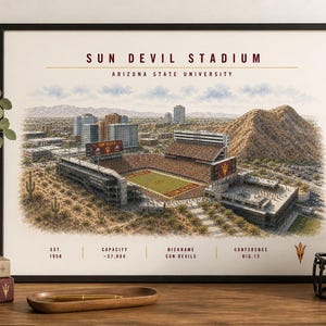 May include: Framed print of Sun Devil Stadium at Arizona State University. The artwork depicts the stadium and surrounding cityscape in a detailed, artistic style. A maroon football helmet with a gold logo sits nearby. The print includes text with the stadium's name, university, and other details.