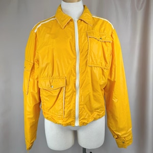May include: Bright yellow jacket with a white zipper and white stripes on the shoulders. The jacket has two front pockets and two chest pockets. The jacket is displayed on a mannequin.
