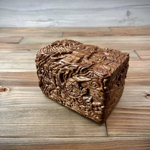 May include: A wooden box with intricate carvings of swirling patterns and designs. The box is made of a dark brown wood and has a smooth, polished finish.