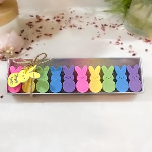 May include: A box of colorful bunny-shaped bath bombs with a yellow tag that says "Happy Easter".