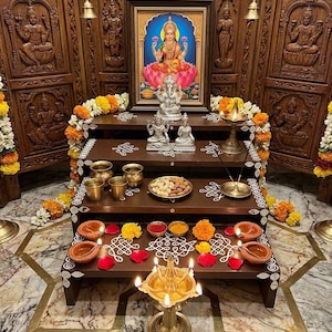 May include: A traditional Hindu altar featuring a framed deity image, silver statues, brass bowls, and lit oil lamps. The altar is adorned with flowers, rose petals, and white and brown patterns.