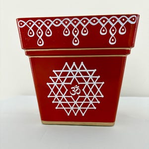 May include: A white ceramic mug with a black handle and the text "But First, Coffee" in a bold, black font. The mug is set against a blurred background, suggesting a cozy setting.