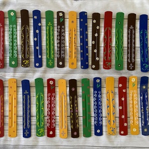 May include: A collection of 30 hand-painted incense sticks with various designs and colors. The sticks are arranged in rows on a light wood surface. Some of the designs include flowers, swirls, and the Om symbol.