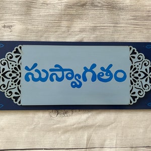 May include: A blue wooden sign with a white background and intricate blue and white designs. The sign says "సమవయం".