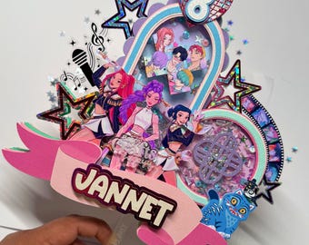 May include: A layered papercraft birthday decoration with the name "JANNET" on a pink banner. The design includes anime-style characters, stars, and a heart-shaped element with the number "8". The color palette is vibrant, featuring pink, blue, and purple.