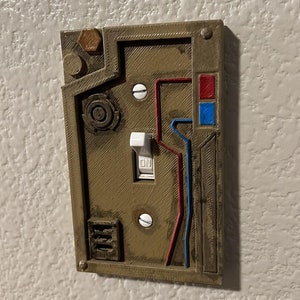 May include: A 3D printed light switch cover with a steampunk design. The cover is brown with red and blue accents. The switch is white and says "ON".