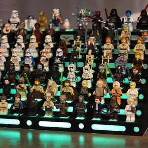 May include: A black display stand with a tiered design, showcasing a collection of Star Wars LEGO minifigures. The stand features a green LED light strip that illuminates the figures.