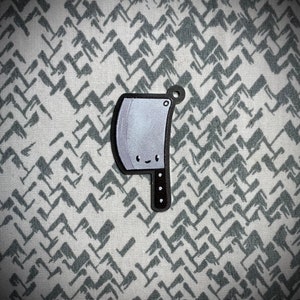 May include: A black and white cartoon cleaver with a smiling face. The cleaver is on a white and gray patterned background.