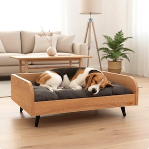 Op de afbeelding: Een houten hondenbed met een donkergrijs kussen. Een beagle slaapt op het bed. Het bed heeft een lichtbruin houten frame en zwarte poten. De hond heeft bruin, zwart en wit haar.