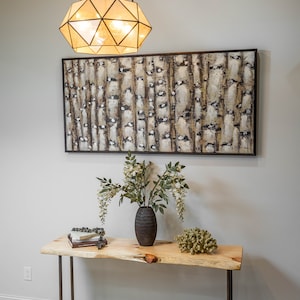 Puede incluir: Una mesa consola de madera con patas de tubo de metal negro. La mesa tiene una tapa de borde vivo y est&aacute; decorada con un jarr&oacute;n de flores blancas, una pila de libros y un trozo de coral. Una l&aacute;mpara geom&eacute;trica cuelga sobre la mesa.