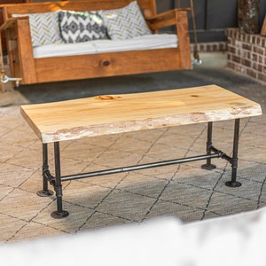 May include: A rustic wooden coffee table with a live edge top and black metal pipe legs. The table is sitting on a patterned rug.