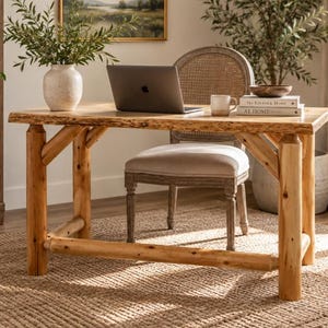 May include: A rectangular wooden desk featuring a natural live edge top and four thick, cylindrical log legs connected by a horizontal support beam. The desk surface is smooth, showcasing the light brown wood grain and raw, textured edges.