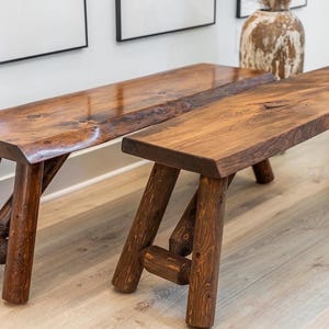 Pode incluir: Dois bancos r&uacute;sticos de madeira com acabamento natural. Os bancos t&ecirc;m uma cor castanha escura e s&atilde;o suportados por pernas angulares em estilo tronco. O gr&atilde;o da madeira &eacute; vis&iacute;vel, adicionando &agrave; est&eacute;tica natural. Adequado para uso interno ou externo.