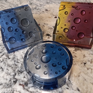 May include: Set of six blue and silver coasters with a moon and craters design, in a clear acrylic holder.  The coasters are stacked on top of each other.