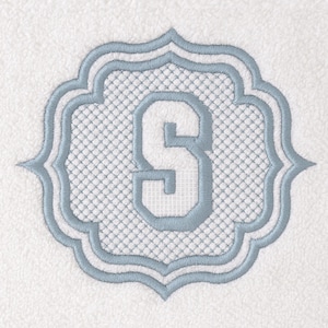 May include: White towel with a light blue embroidered monogram. The monogram is the letter "S" inside a decorative frame with a lattice pattern. The towel has a textured surface.