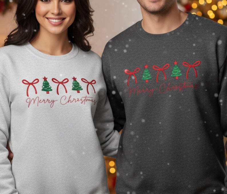 May include: Two sweatshirts, one light grey and one charcoal, feature a festive design. Each has red bows, green Christmas trees, and the words "Merry Christmas" in a script font. Ideal for the holiday season.