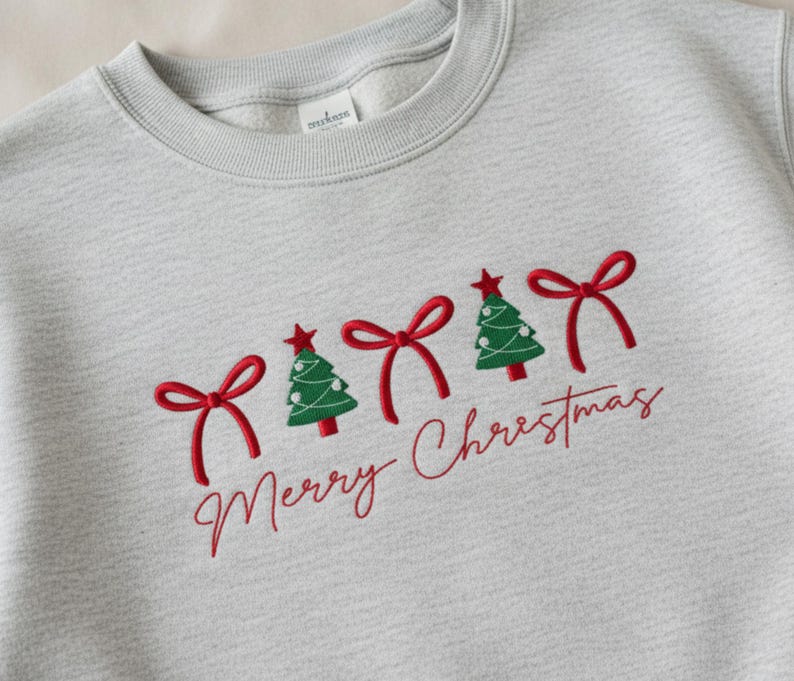 May include: Pale grey sweatshirt featuring red embroidered bows, green Christmas trees, and the words "Merry Christmas" in red script. The trees are topped with red stars.