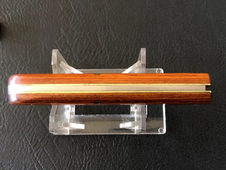 May include: A wooden knife with a brass accent, displayed on a clear acrylic stand. The knife has a dark brown handle and a light brown blade. The brass accent runs along the length of the knife.