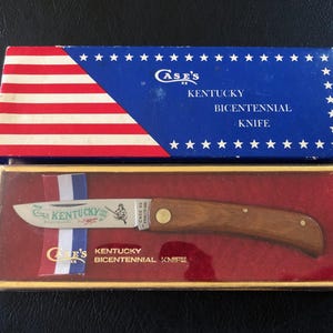 May include: A vintage Case's Kentucky Bicentennial Knife in its original box. The box features a blue top with white stars and red and white stripes. The knife has a wooden handle and a blade with the words "Case's Kentucky" and an illustration.