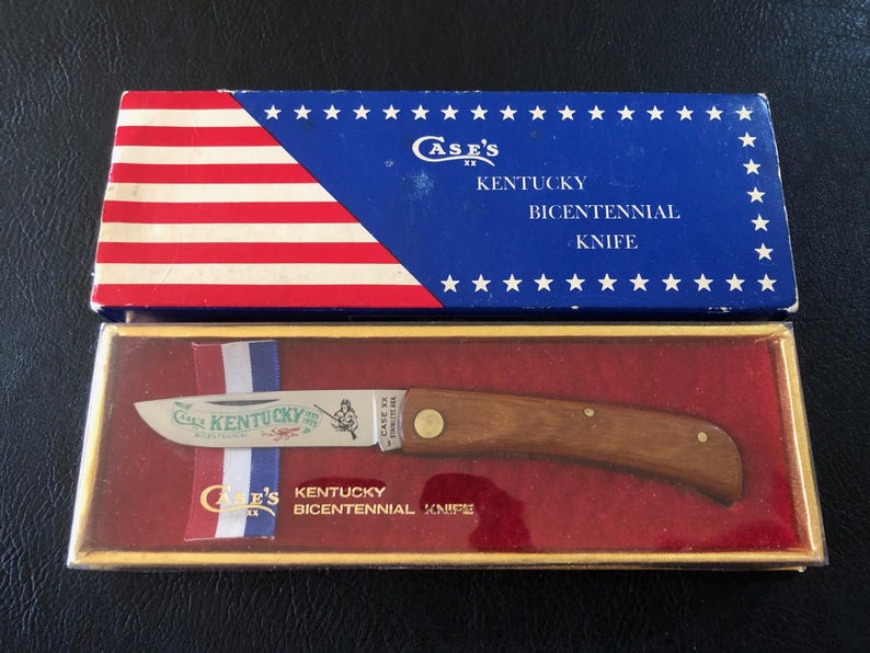 May include: A vintage Case's Kentucky Bicentennial Knife in its original box. The box features a blue top with white stars and red and white stripes. The knife has a wooden handle and a blade with the words "Case's Kentucky" and an illustration.