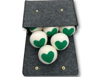 May include: A gray felt bag with a zipper opening, containing white wool dryer balls with green heart designs. The bag has the text "OBVIOUSLYFAB" printed on the front.