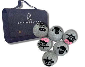 May include: A set of six gray felt dryer balls with black and pink animal faces. The balls are in a gray felt bag with the text "OBVIOUSLY FAB" printed on it.