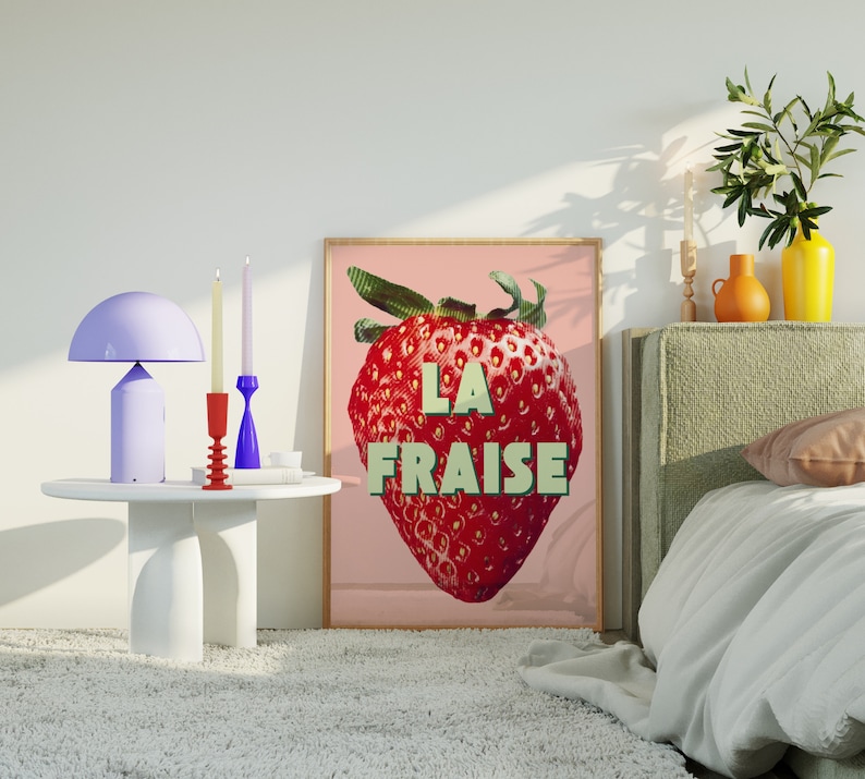 K&ouml;nnte beinhalten: Ein rosa-wei&szlig;es Poster mit einer gro&szlig;en roten Erdbeerillustration und dem Text "LA FRAISE". Das Poster h&auml;ngt an einer wei&szlig;en Wand &uuml;ber einem Bett mit einem gr&uuml;nen Kopfteil.