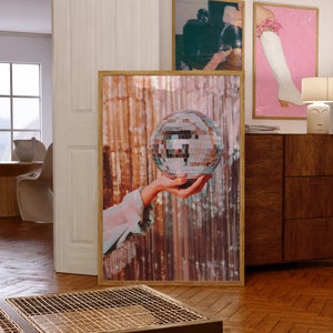 May include: A hand holding a silver disco ball in front of a shimmering gold background.