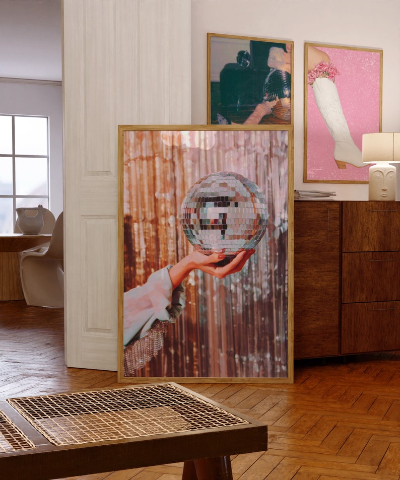 May include: A hand holding a silver disco ball in front of a shimmering gold background.