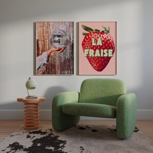 K&ouml;nnte beinhalten: Zwei gerahmte Drucke h&auml;ngen an einer wei&szlig;en Wand. Der Druck links zeigt eine Hand, die eine Discokugel h&auml;lt. Der Druck rechts zeigt eine rote Erdbeere mit dem Text "LA FRAISE" in gr&uuml;nen Buchstaben.