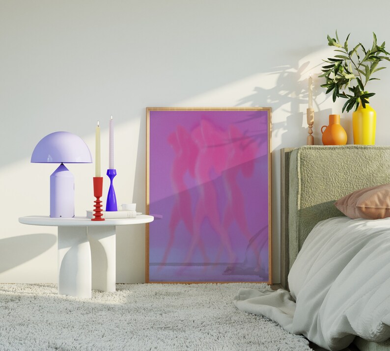 May include: A white table with three candlesticks and a purple lamp. The candlesticks are red and blue. The lamp has a white shade. There is a framed picture of two figures in a purple and pink color scheme behind the table.
