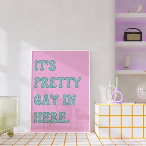 May include: A pink poster with the text "It's Pretty Gay In Here." in teal lettering.