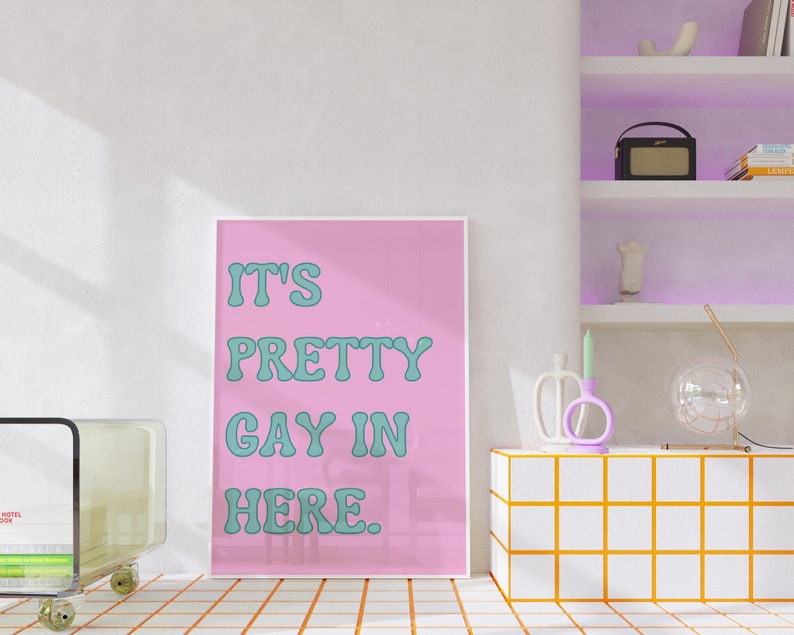 May include: A pink poster with the text "It's Pretty Gay In Here." in teal lettering.