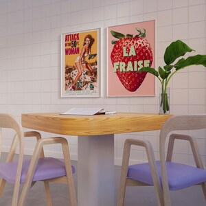 K&ouml;nnte beinhalten: Ein Holztisch mit einem wei&szlig;en Untergestell und zwei hellvioletten St&uuml;hlen. Auf dem Tisch liegt ein Magazin. An der Wand hinter dem Tisch h&auml;ngen zwei gerahmte Poster. Ein Poster zeigt eine Frau im Badeanzug und das andere Poster zeigt eine Erdbeere mit dem Text "LA FRAISE".