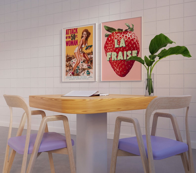 K&ouml;nnte beinhalten: Ein Holztisch mit einem wei&szlig;en Untergestell und zwei hellvioletten St&uuml;hlen. Auf dem Tisch liegt ein Magazin. An der Wand hinter dem Tisch h&auml;ngen zwei gerahmte Poster. Ein Poster zeigt eine Frau im Badeanzug und das andere Poster zeigt eine Erdbeere mit dem Text "LA FRAISE".