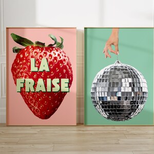 K&ouml;nnte beinhalten: Zwei gerahmte Drucke, einer mit einer roten Erdbeere mit dem Text "LA FRAISE" auf rosa Hintergrund und der andere mit einer silbernen Discokugel, die an einer Hand an einem hellgr&uuml;nen Hintergrund h&auml;ngt.