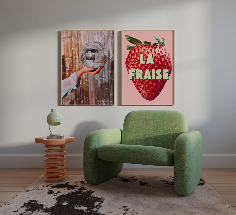 May include: Two framed prints hanging on a white wall. The print on the left shows a hand holding a disco ball. The print on the right shows a red strawberry with the text "LA FRAISE" in green letters.